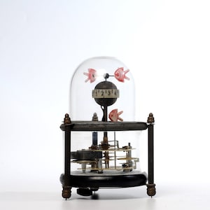 May include: A vintage clock with a glass dome and a intricate gear mechanism. The clock features a small, round face with black numbers and a red and white fish design. The clock is encased in a clear glass dome with a brass base.