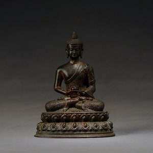 Op de afbeelding: Een donker bronzen beeld van een zittende Boeddha met een gedetailleerde lotusbasis. De Boeddha zit in meditatieve houding met de handen in de schoot.