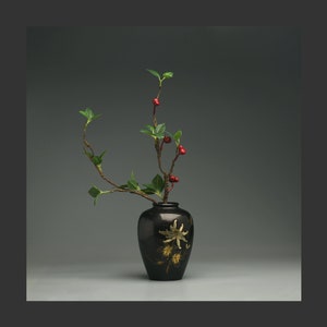Peut inclure: Une seule branche avec des feuilles vertes et des baies rouges disposées dans un vase noir avec des motifs floraux dorés.