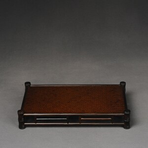 Puede incluir: Un expositor de madera marr&oacute;n oscuro con una parte superior tejida y una forma rectangular. El expositor tiene un dise&ntilde;o sencillo con cuatro patas y un marco alrededor de la parte superior.