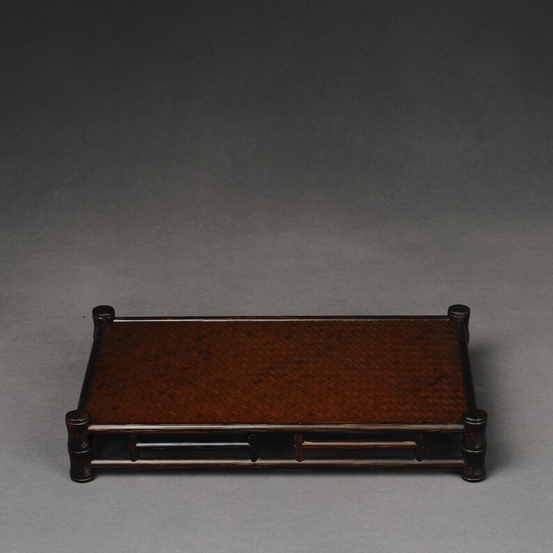 Puede incluir: Un expositor de madera marr&oacute;n oscuro con una parte superior tejida y una forma rectangular. El expositor tiene un dise&ntilde;o sencillo con cuatro patas y un marco alrededor de la parte superior.