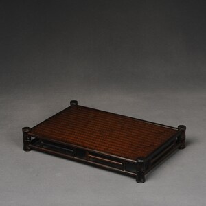 Puede incluir: Un expositor de madera marr&oacute;n oscuro con una parte superior tejida y una forma rectangular. El expositor tiene cuatro patas y un dise&ntilde;o sencillo.