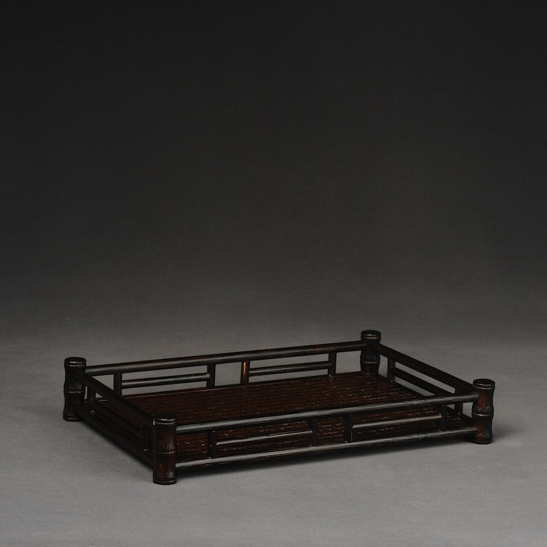 Puede incluir: Una bandeja rectangular de bamb&uacute; marr&oacute;n oscuro con un fondo tejido y un borde elevado. La bandeja est&aacute; hecha de bamb&uacute; natural y tiene un aspecto r&uacute;stico y artesanal.