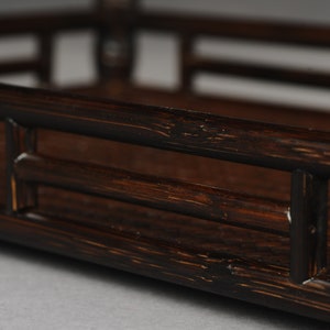 Puede incluir: Una bandeja rectangular de color marr&oacute;n oscuro hecha de bamb&uacute; tejido con un borde elevado. La bandeja tiene un dise&ntilde;o sencillo con unas pocas lamas horizontales.