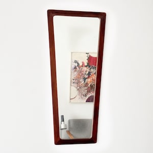 May include: A tall, rectangular mirror with a dark wood frame. The frame has a unique, slightly angled design. The mirror reflects a painting and a lamp.