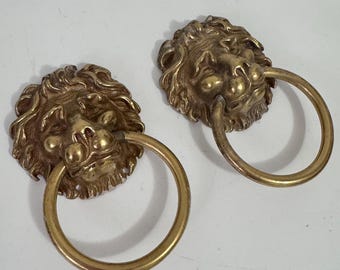 Könnte beinhalten: Zwei antike Türklopfer aus Messing in Form eines Löwenkopfes. Jeder Klopfer hat einen detaillierten Löwenkopf mit einem Ringgriff. Das Messing hat eine warme, gealterte Patina. Für eine Haustür oder einen Schrank.