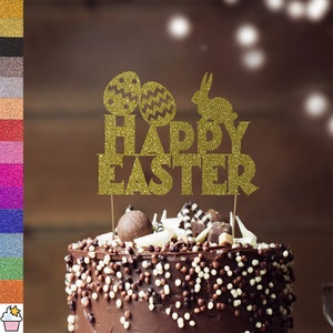 May include: A gold glitter "Happy Easter" cake topper with two decorated eggs and a rabbit silhouette. The topper sits on a chocolate cake with white and brown sprinkles and chocolate decorations. A festive Easter cake decoration.