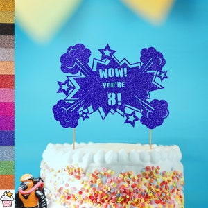 Może przedstawiać: Niebieski topper na tort z brokatem na białym tle. Topper ma kształt komiksowej eksplozji z tekstem "WOW! YOU'RE 8!"