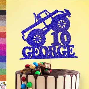 Può includere: Topper per torta blu glitterato con un design di monster truck, il numero 10 e il nome George. Il topper è su una torta con glassa al cioccolato e caramelle colorate.