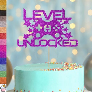 Puede incluir: Topper de pastel de purpurina morada con el texto "Nivel 18 Desbloqueado" y un mando de videojuego de purpurina morada.