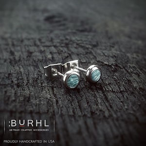 May include: A pair of silver stud earrings featuring small, circular, light blue textured inlays. The earrings have a polished metal setting and a standard post back. The text :BURHL ARTISAN CRAFTED ACCESSORIES PROUDLY HANDCRAFTED IN USA is visible.