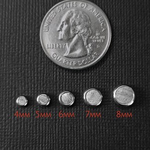 以下が含まれることがあります： 直径4mmから8mmのテクスチャ加工された中心部を持つ5つの円形シルバー調金属ベゼルが並んでおり、比較用にアメリカの25セント硬貨が置かれています。各パーツの下には4mm、5mm、6mm、7mm、8mmのサイズを示すテキストラベルが記載されています。