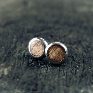 May include: A pair of silver stud earrings with a round wooden inlay. The wood has a light brown color and a natural grain pattern.