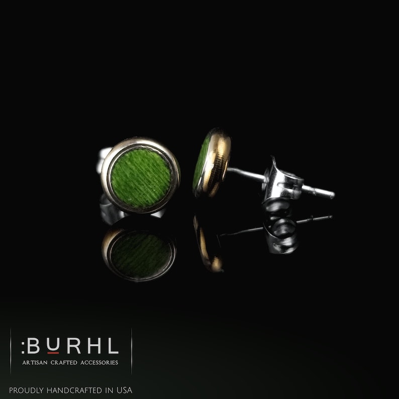 May include: A pair of round stud earrings featuring a vibrant green textured center inlay surrounded by a metallic rim. The earrings include standard post backs and are displayed against a black background with the text :BURHL ARTISAN CRAFTED ACCESSORIES PROUDLY HANDCRAFTED IN USA.