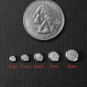 May include: Five circular metal bezels with textured centers arranged in a row, labeled 4mm, 5mm, 6mm, 7mm, and 8mm. A United States quarter dollar coin is positioned above the bezels for scale. The text BURHL ARTISAN CRAFTED ACCESSORIES is visible.