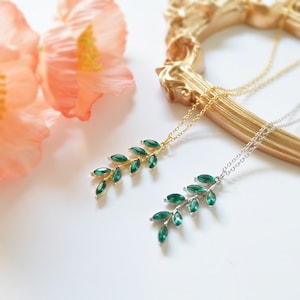 May include: Two delicate necklaces with green gemstone leaf pendants. One necklace has a gold chain and the other has a silver chain.