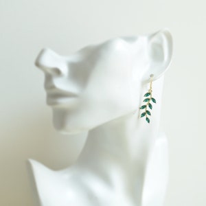 May include: Gold dangle earrings with a green leaf design. The leaves are made of faceted glass.