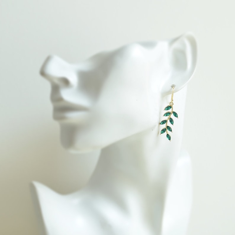 May include: Gold dangle earrings with a green leaf design. The leaves are made of faceted glass.