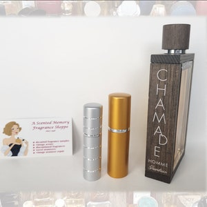 May include: The image displays a perfume bottle and two travel atomisers. The perfume bottle is rectangular with a wooden exterior and the word "CHAMADE HOMME" in white. The atomisers are silver and gold. A business card for "A Scented Memory Fragrance Shoppe" is also present.