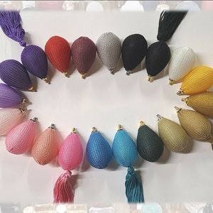 May include: A selection of vintage perfume atomisers in a rainbow of colours, including purple, red, pink, blue, and gold. Each atomiser has a bulbous shape, a gold-coloured metal top, and a matching tassel. The atomisers are arranged in a circular pattern.