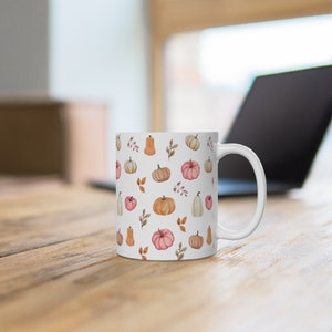 May include: White ceramic mug with a pattern of orange, pink, and white pumpkins and leaves. The mug has a white handle.