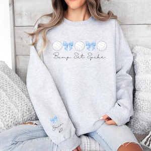 May include: Gray sweatshirt with a volleyball graphic and the text "Bump. Set. Spike."  The sleeve has a blue bow and the text "Erin #17".