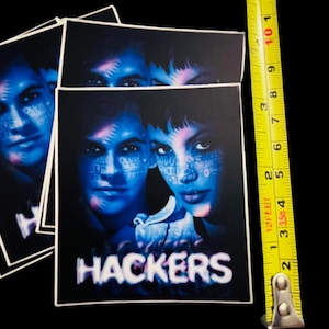 May include: A blue and purple sticker with a movie poster design featuring two people's faces. The text "HACKERS" is printed in white letters on the sticker.
