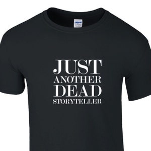 Peut inclure: T-shirt noir avec du texte blanc qui dit "Just Another Dead Storyteller".