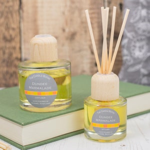 May include: Two glass diffuser bottles with wooden caps and reeds. Both bottles contain a yellow liquid and have labels that read "The Candle  Bothy Dundee Marmalade Diffuser Handmade in Dundee, Scotland".