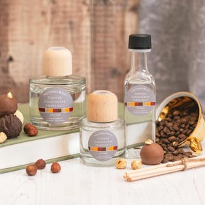 May include: Three glass bottles of diffuser oil with wooden caps. The bottles are labelled "Coffee Chocolate Hazelnut". The bottles are surrounded by coffee beans, chocolate truffles, and hazelnuts.