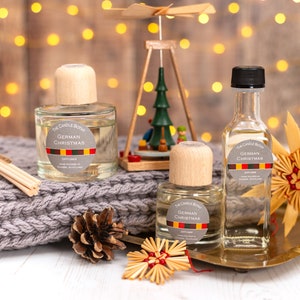 May include: Three glass bottles of German Christmas diffuser oil with wooden caps. The bottles are on a wooden tray with a straw star and a pine cone. The bottles have a label that says "The Candle Botany German Christmas Diffuser".