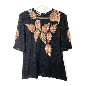 May include: A black sequined top with a gold and copper leaf design. The top has a scoop neck and short sleeves.