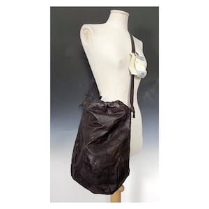 Può includere: Una borsa a sacchetto in pelle marrone con un design a patchwork. La borsa ha una lunga tracolla ed è esposta su un manichino.