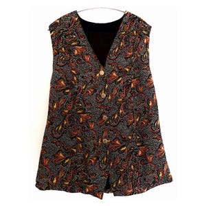 May include: A sleeveless vest with a black paisley pattern featuring red and gold accents. The vest has a V-neck, gold buttons, and a black lining. The fabric has a textured appearance, and the vest is hanging on a silver hanger.