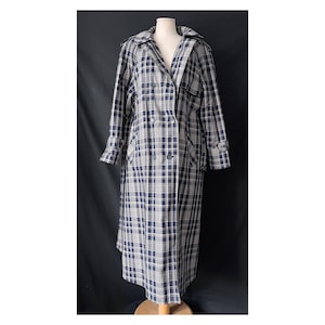 May include: A long, double-breasted trench coat in a navy blue and white plaid pattern. The coat features a classic collar, shoulder epaulets, and a matching belt. The coat is displayed on a mannequin.