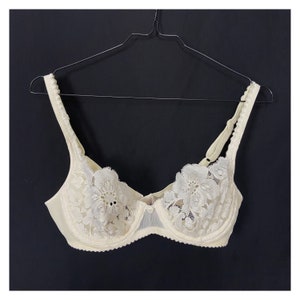 May include: A white lace bra with floral detailing. The bra has adjustable straps and a hook and eye closure in the back.