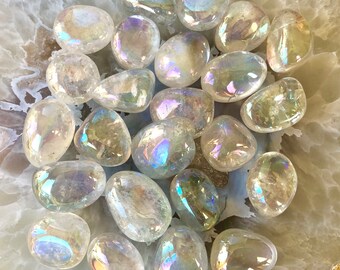 May include: A collection of iridescent clear quartz tumbled stones. The stones are smooth and polished, with a rainbow sheen.