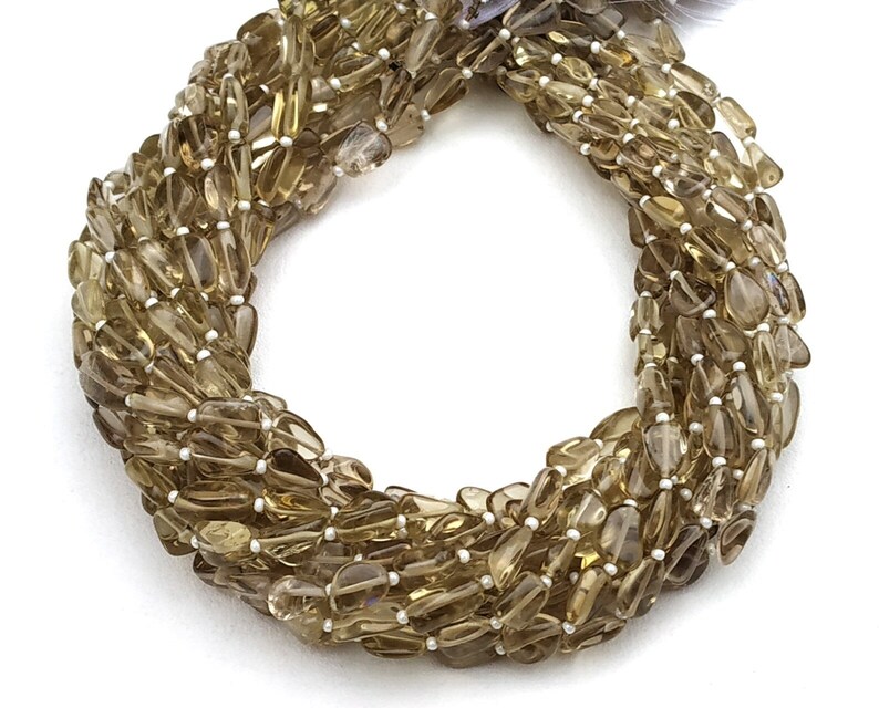 May include: A strand of brown smoky quartz gemstone beads, each bead is a teardrop shape with a faceted finish. The beads are strung on a clear thread.