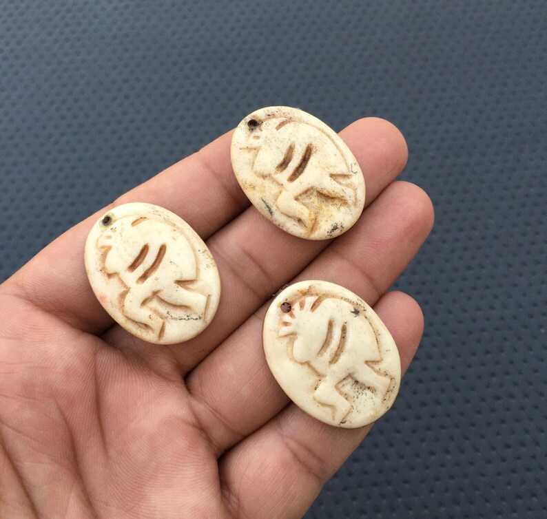May include: Three oval-shaped bone pendants with a carved design of a stylized animal. The pendants are off-white with a slightly yellowed hue.