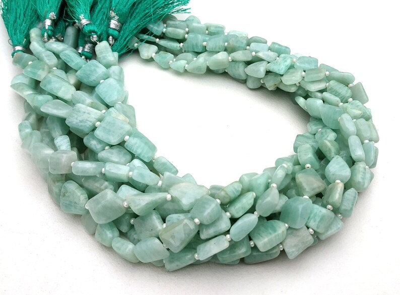 May include: A strand of light green aquamarine gemstone beads. The beads are faceted and have a slightly irregular shape. The beads are strung on a clear thread and are ready to be used for jewelry making.