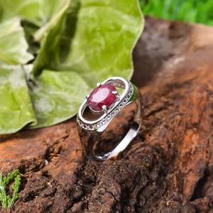 May include: A silver ring with a red oval gemstone set in a delicate, open-work design. The ring is accented with small, clear gemstones.