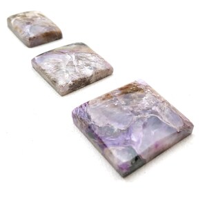 May include: Three square-shaped purple and grey gemstone cabochons of varying sizes, arranged in a row from largest to smallest.