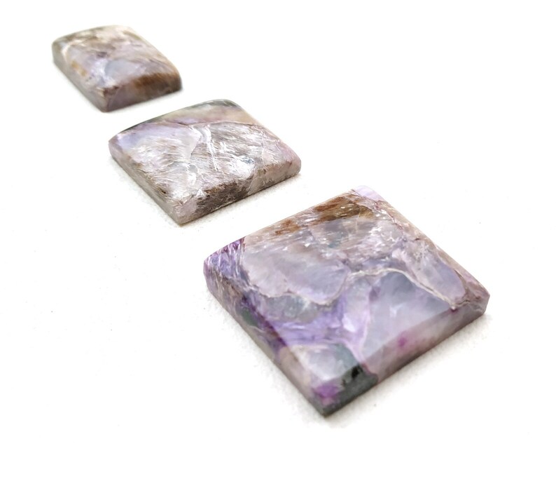 May include: Three square-shaped purple and grey gemstone cabochons of varying sizes, arranged in a row from largest to smallest.
