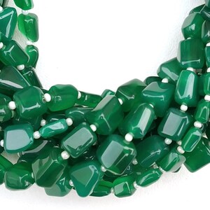 May include: A strand of green gemstone beads, likely jade or aventurine, with a smooth, polished finish. The beads are irregularly shaped and have a slightly rectangular form. The beads are strung on a white thread or cord.