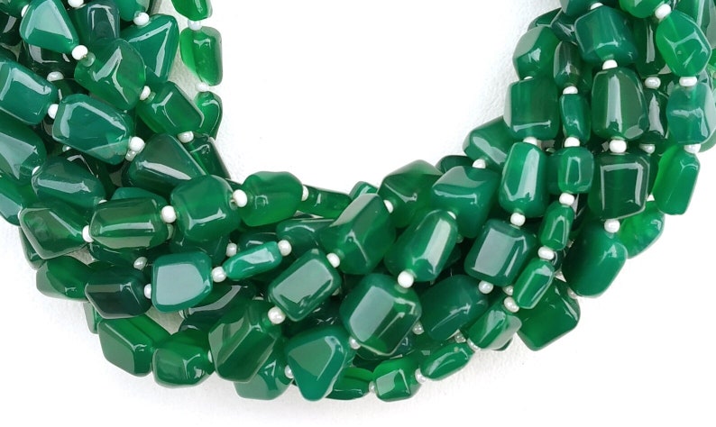 May include: A strand of green gemstone beads, likely jade or aventurine, with a smooth, polished finish. The beads are irregularly shaped and have a slightly rectangular form. The beads are strung on a white thread or cord.
