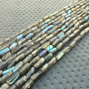 May include: A strand of grey and blue labradorite gemstone beads. The beads are faceted and have a rectangular shape.