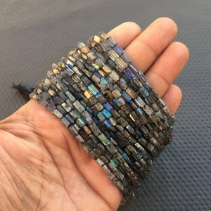 May include: A strand of dark gray faceted labradorite beads with iridescent blue and green flashes. The beads are rectangular in shape and have a smooth, polished finish.
