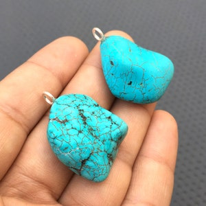 Può includere: Due ciondoli in pietra turchese blu con anelli a salto in argento. Le pietre hanno una texture ruvida e naturale e un motivo screziato.