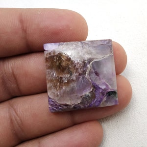 May include: A square-shaped purple and brown gemstone with a unique, swirling pattern. The gemstone is cut and polished, and it has a smooth, glossy finish.