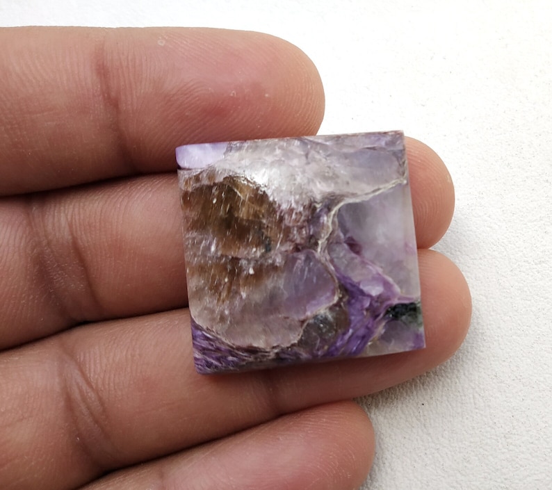 May include: A square-shaped purple and brown gemstone with a unique, swirling pattern. The gemstone is cut and polished, and it has a smooth, glossy finish.